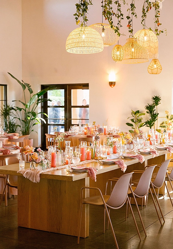 Reception tablescape with a long table wedding reception setup, tapered candles and floral bud vases under rattan pendant lights indoors
