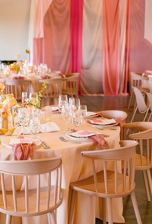 Reception tablescape with round wedding table setup in blush linens, candlelit florals, menus and place cards, plus draped fabric backdrop in modern space