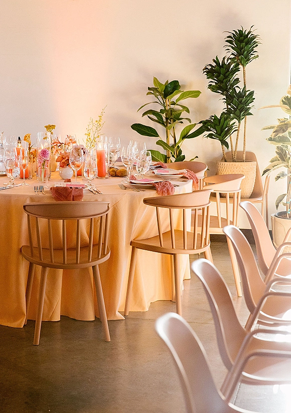 Reception tablescape on a round wedding reception table with beige linens, blush napkins, pink taper candles, bud vases, and bread rolls indoors