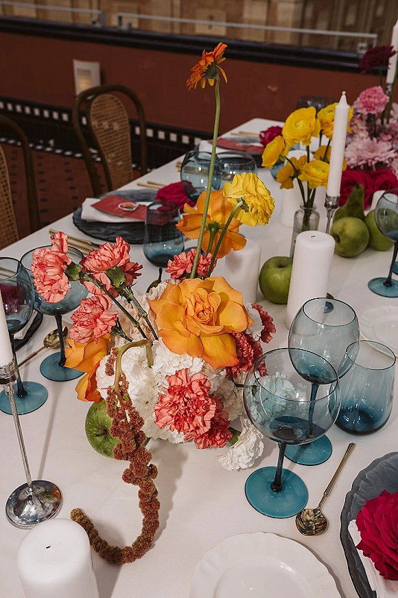 Reception tablescape with colorful wedding tablescape florals, blue glass goblets, gold flatware, and candlelight in a chic restaurant interior