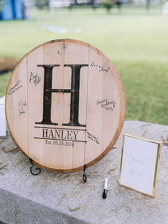 Wedding guest book displayed as a wood guest book alternative round monogram sign on a black stand, with marker on a stone ledge outdoors