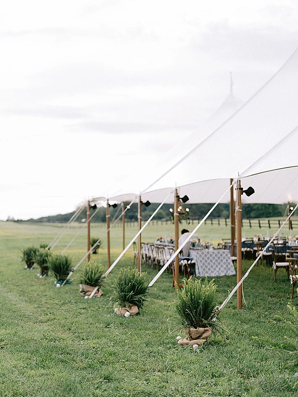 Outdoor reception tent with sailcloth wedding tent details, bistro string lights over long banquet tables set in a grassy field with hills