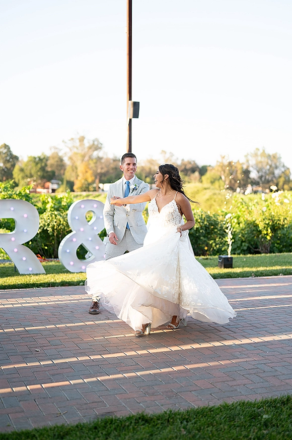 First dance moment outdoors as the bride twirls her wedding gown with the groom, framed by marquee letter lights and cold spark fountains