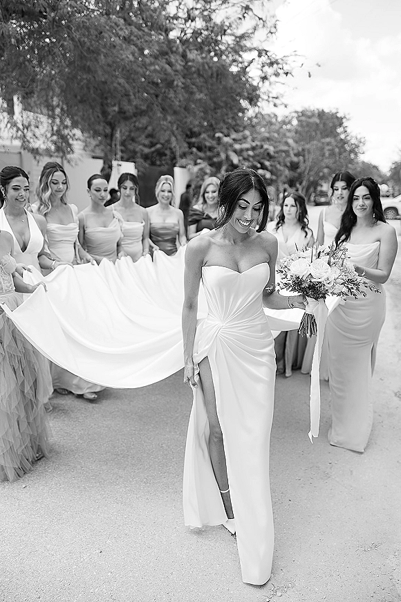 Bride portrait in a black and white wedding photo, holding a ribbon-tied bouquet in a strapless slit gown on a tree-lined street