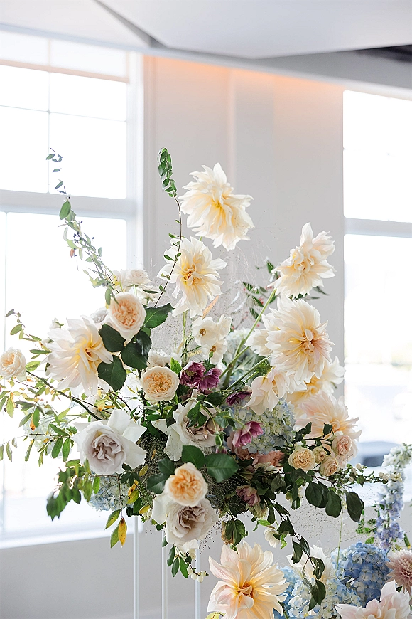 Wedding floral arrangement statement floral centerpiece with dahlias and garden roses in soft daylight by large windows indoors