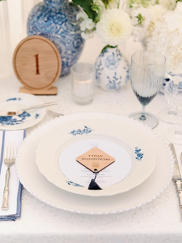 Reception tablescape with blue and white wedding table china, menu card and tassel place card, blue goblet, and white florals on patterned cloth