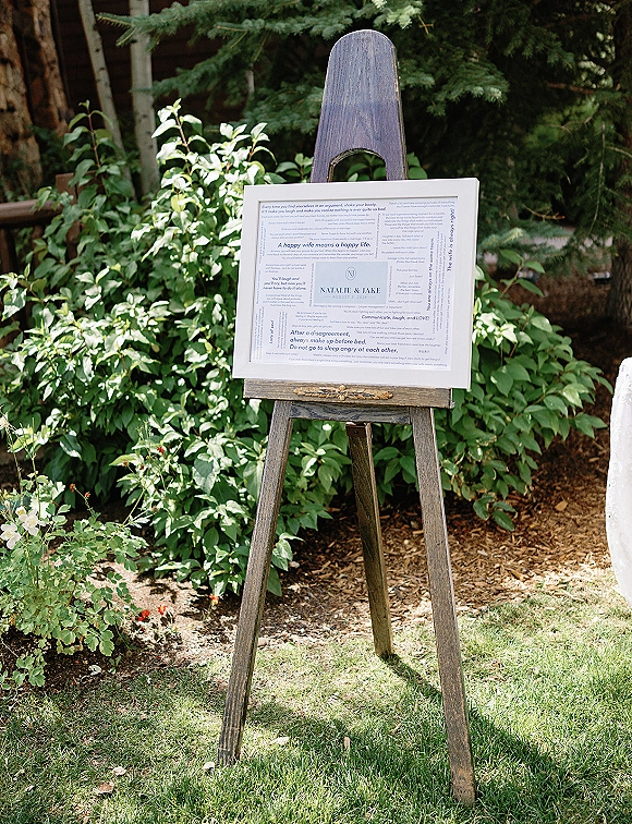 Wedding welcome sign on easel in a framed print, set on a grassy lawn with garden greenery and trees behind