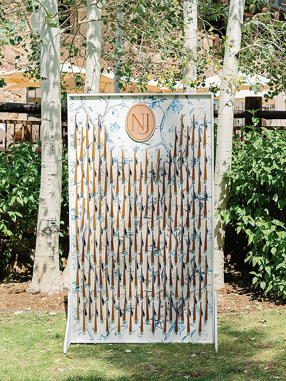 Wedding seating chart with escort card display, monogram and framed board on a stand, set against aspen trees in an outdoor garden lawn