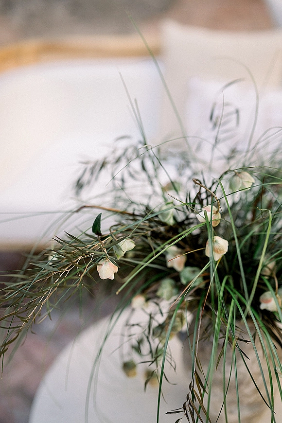 Wedding bouquet with airy greenery and delicate white blooms, long grass and trailing foliage against a softly blurred neutral backdrop