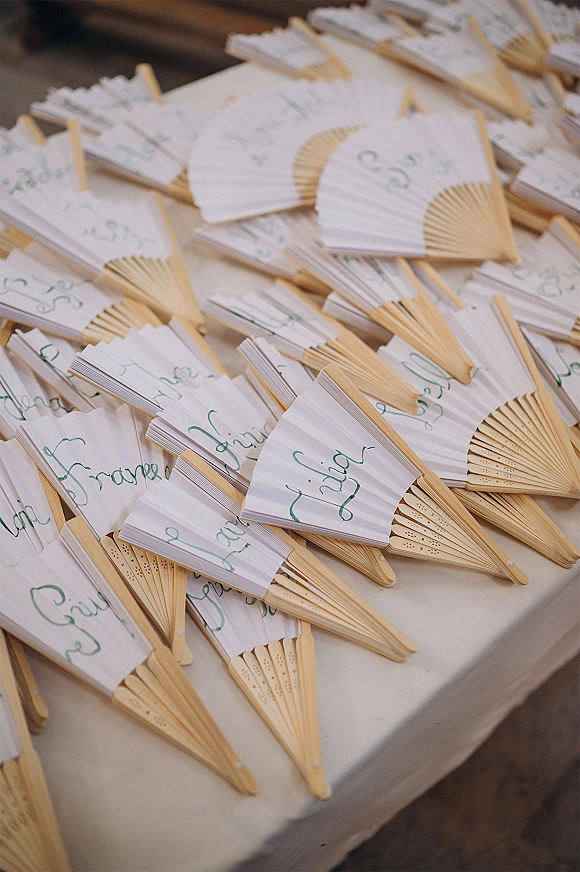 Wedding favor fans with custom wedding hand fans in white paper, bamboo handles, and green calligraphy lettering on a linen tablecloth