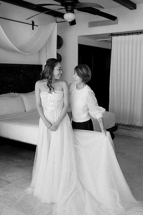 Bride getting ready in a strapless lace gown as her long veil drapes over the bed in a bedroom bridal suite with curtains and beams