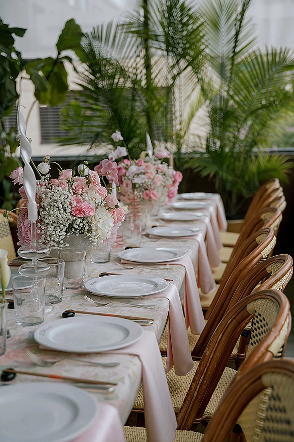 Reception tablescape with pink wedding tablescape florals, white taper candles, blush runner and patterned cloth on an outdoor patio with palms.