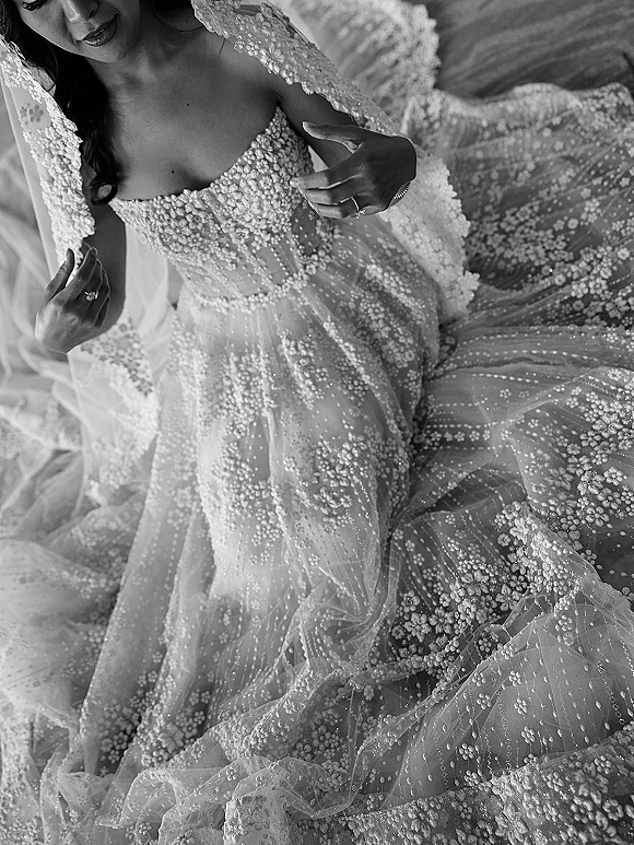 Wedding dress close-up of a beaded wedding dress with floral appliqué, sheer corset bodice, tulle skirt, veil and rings on bed sheets