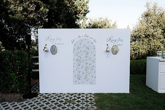 Wedding ring box display stand with calligraphy name labels and bells on white panels, set on garden lawn by walkway pavers