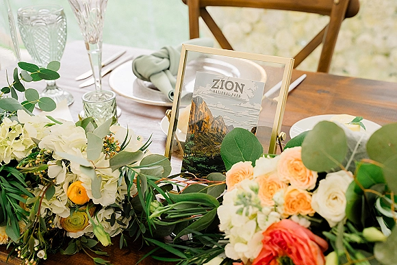 Wedding tablescape with a wedding table centerpiece garland of roses and hydrangeas, gold-framed table number, and elegant place settings on rustic wood table