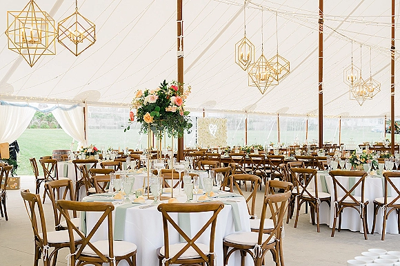 Reception tablescape with round wedding tables, light blue runners, taper candles, tall florals, and string lights under a draped white tent canopy