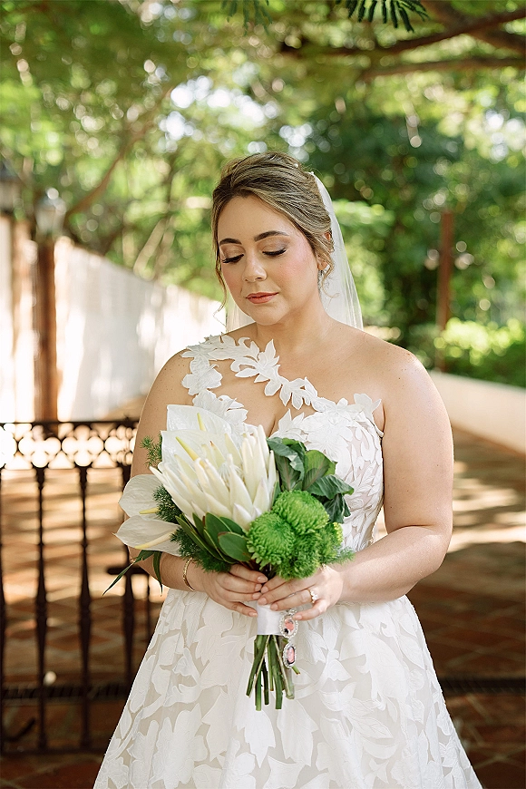 Bridal portrait of a bride holding bouquet in a strapless lace wedding dress, looking down with veil in an outdoor garden patio setting
