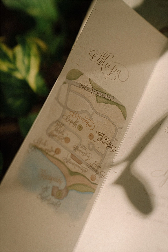 Wedding invitation suite with custom wedding map card, calligraphy details, and paper pieces styled on green foliage in sunlit shadows