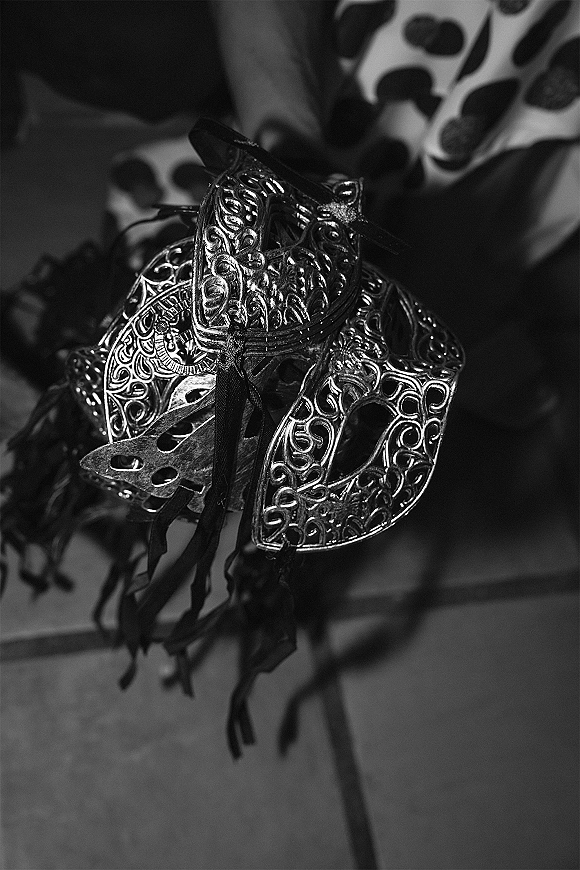 Wedding bouquet detail with bouquet charm featuring ornate metal filigree and ribbon ties, set against patterned fabric and floor tiles