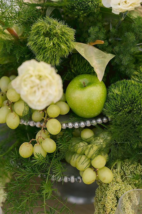 Wedding centerpiece with a green apple centerpiece of grapes, white flowers, and greenery, finished with a beaded garland on the table surface