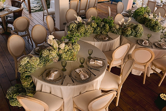 Reception tablescape with round wedding reception tables, ivory linens, hydrangea garland and white anthurium centerpieces on a waterfront deck