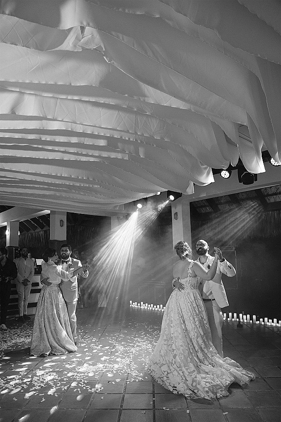 First dance as bride and groom sway on the wedding reception dance floor, candlelit with confetti and draped ceiling above guests