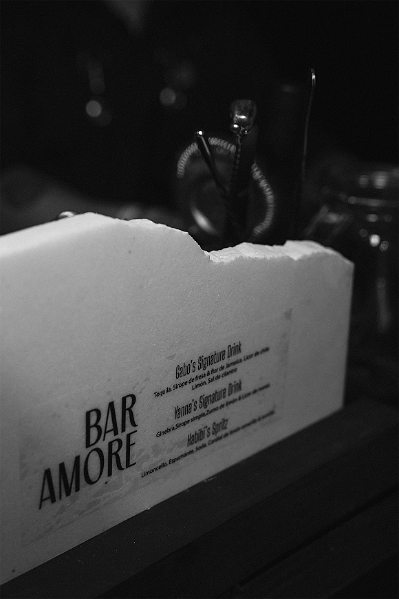 Wedding bar menu and signature cocktails sign on a dark reception bar counter, with bottles and bar tools behind the menu card