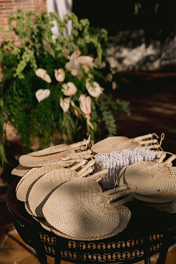 Wedding favor fans and palm fan wedding favors displayed with bubble wands and greenery on a patio table against a brick wall backdrop
