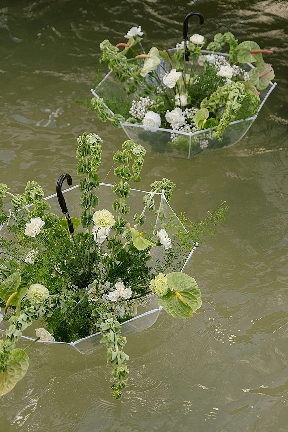 Floating wedding florals with umbrella floral arrangement of white blooms, anthurium, and trailing greenery drifting on rippling water