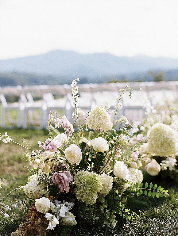 Ceremony aisle flowers in an aisle floral arrangement of white and blush roses, hydrangea, and greenery on a lawn with mountain views