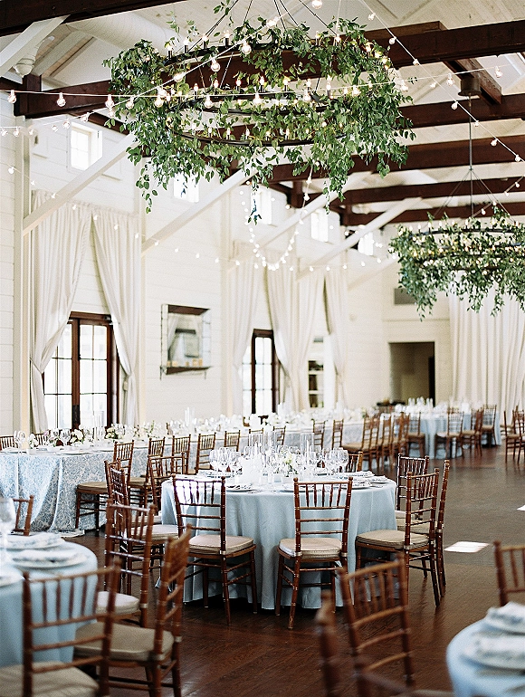 Reception tablescape with a wedding reception table setup featuring light blue linens, floral centerpieces, and greenery chandelier under string lights