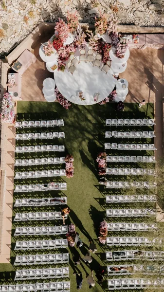 Ceremony setup with an outdoor wedding ceremony layout of white folding chairs circling a round platform, pink and purple florals on a green lawn