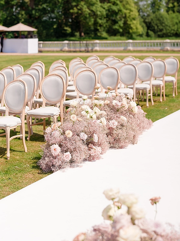 Ceremony aisle decor with outdoor ceremony aisle, a white aisle runner flanked by blush roses and baby's breath on a grassy lawn with trees