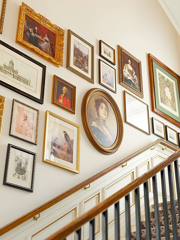 Staircase gallery wall with staircase wall art in gold frames and an oval portrait, lined along a white stairwell with banister and runner