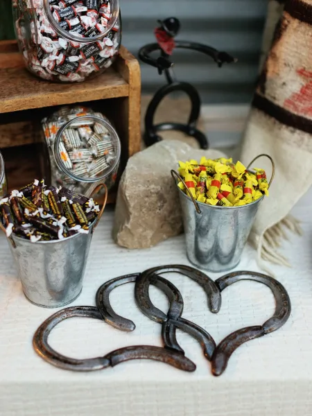 Wedding candy bar with glass candy jars and rustic candy display featuring metal pails, horseshoes, and wrapped sweets on a white tablecloth