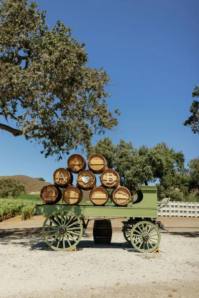 Wedding welcome display with barrel wedding decor, wooden monogram letters and heart cutout on a vintage wagon along vineyard rows
