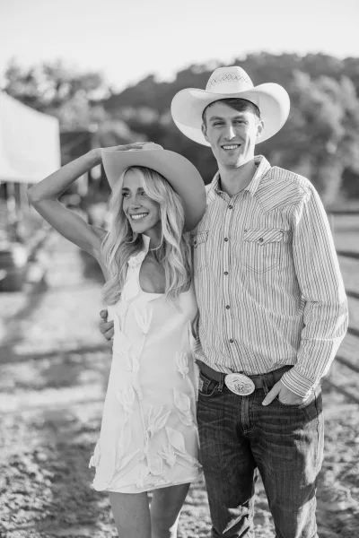Couple portrait of a western wedding couple in cowboy hats, bride in short wedding dress and groom in jeans on a sunlit ranch path