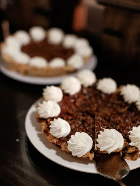 Wedding dessert slice of chocolate pie topped with whipped cream dollops on a plate, pie server beside it on a dark table backdrop