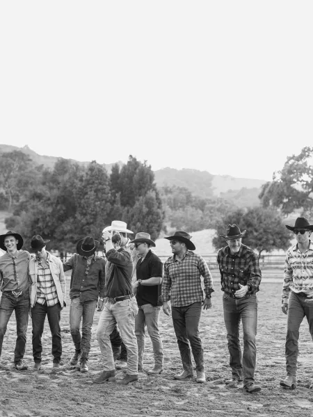 Groomsmen portrait of men in cowboy hats walking in plaid shirts, jeans and boots, with mountains, ranch fence and open sky behind them