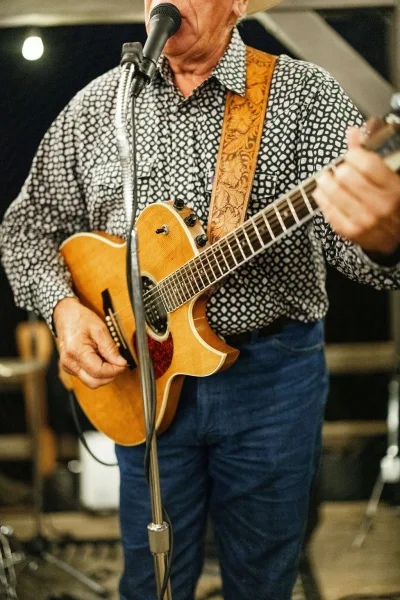 Wedding live music performer in a patterned shirt playing acoustic guitar at a microphone on an indoor stage with lights