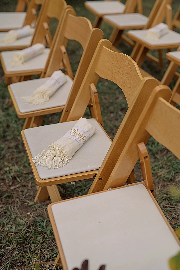 Ceremony seating with outdoor ceremony chairs in wood folding rows, cushions and welcome blankets on chair backs across a grassy lawn