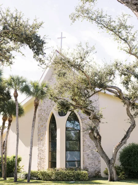 Church wedding venue, a chapel wedding venue with arched windows, framed by palm trees and a green lawn under a bright blue sky.