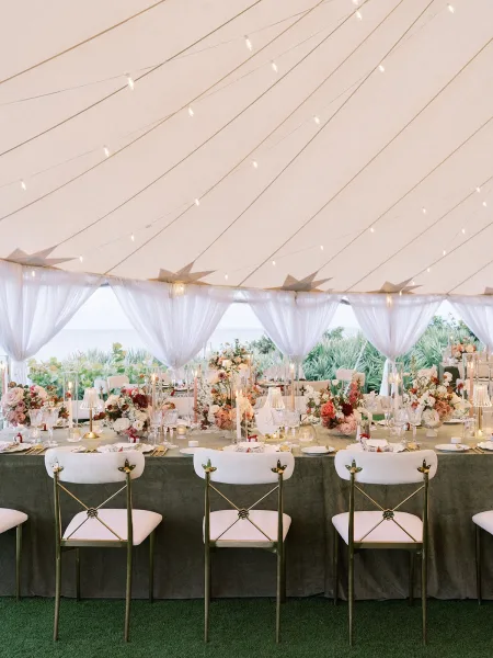 Reception tablescape with tented reception decor, a warm candlelit glow along the table under a sheer tent canopy facing the ocean.