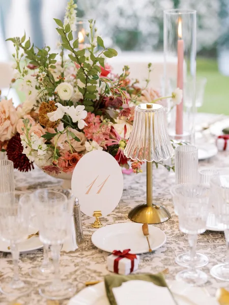 Reception tablescape on a garden wedding table, accented by pink taper candles, set amid garden greenery on a lawn.
