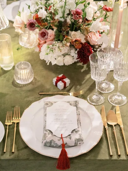Wedding place setting with a gold flatware setting and a menu card centered on the dinner plate, styled for an elegant reception.