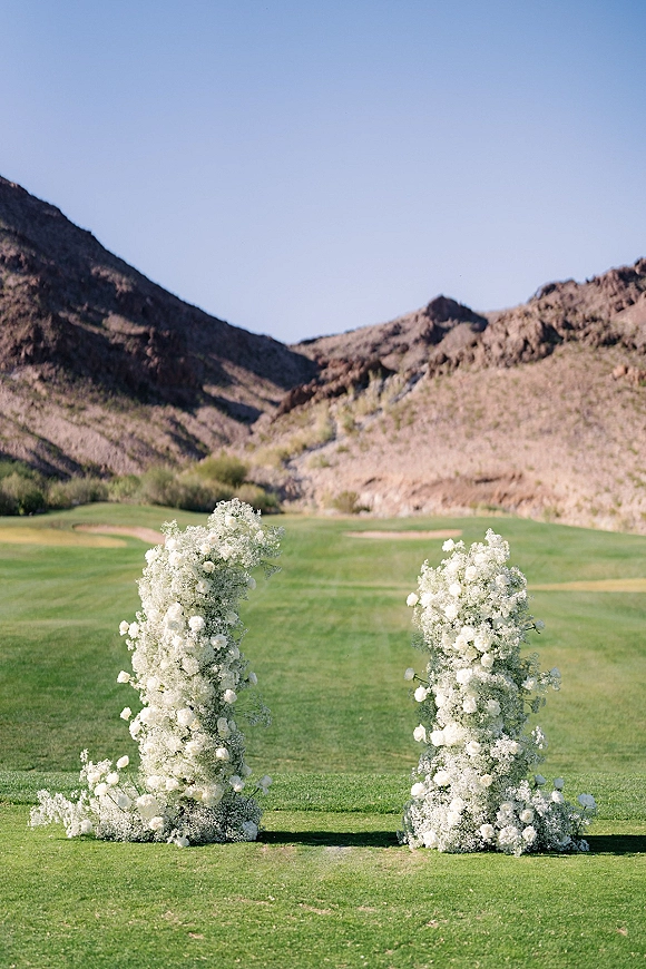 Wedding ceremony altar with outdoor wedding altar white floral pillars of roses and baby's breath on a grassy lawn with mountains beyond