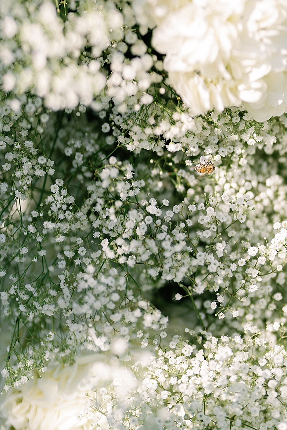 Wedding flowers close-up featuring baby’s breath, white roses, and greenery accents against a soft green foliage background