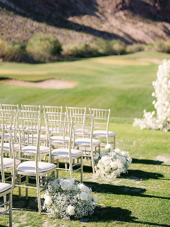 Outdoor ceremony seating with chiavari chair ceremony rows lining a grassy aisle, dotted with white rose and baby's breath markers on a lawn