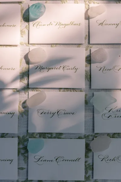 Wedding place cards with calligraphy place cards and sea glass accents arranged on a patterned tablecloth for reception seating display