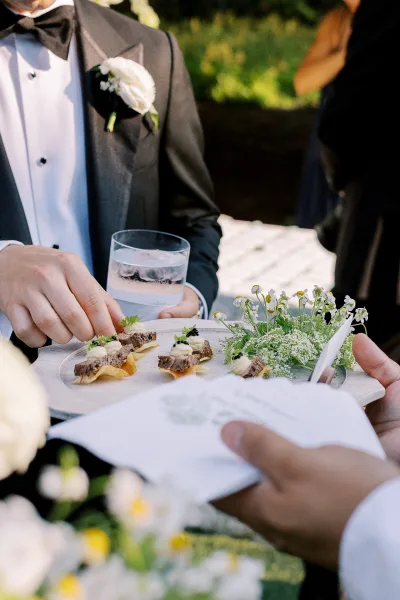 Cocktail hour appetizers on a passed hors doeuvres wedding tray, canapés topped with microgreens held by tuxedoed server outdoors
